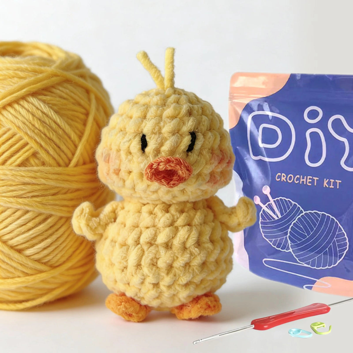 A yellow crocheted bird toy next to a purple bag of crochet kit supplies and a needle.