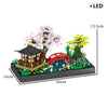 A miniature landscape featuring a traditional Japanese treehouse with pink blossoms, green trees, and a red bridge, illuminat