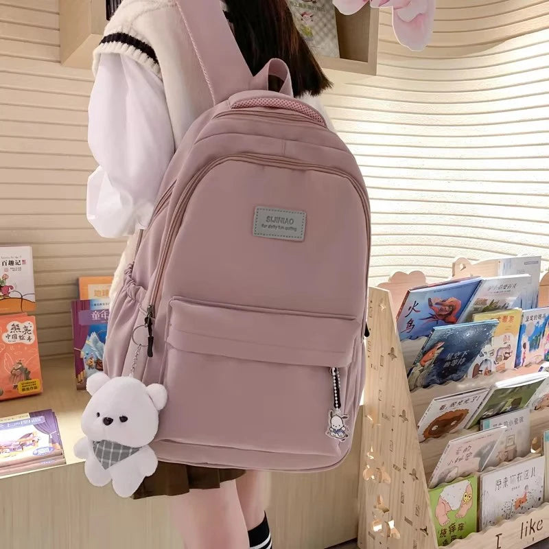 A pink waterproof nylon laptop backpack with a white bear charm is shown in a vertical shot.