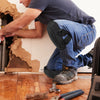 A person wearing blue jeans is kneeling and working on a wooden floor, with black knee pads visible.