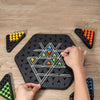 A hand is placing a black jumping board game with white lines and colored pegs onto a wooden surface.
