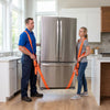 Two people using orange adjustable furniture moving straps to secure a large stainless steel refrigerator.