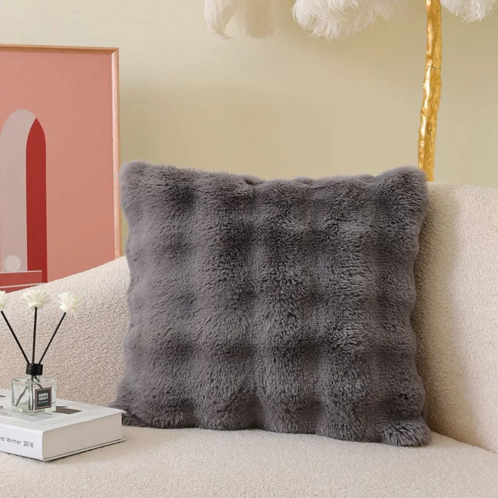 A gray fluffy decorative pillow cover resting on a light-colored sofa.