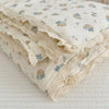 A stack of floral muslin baby blankets in cream and blue floral patterns folded on a white surface.