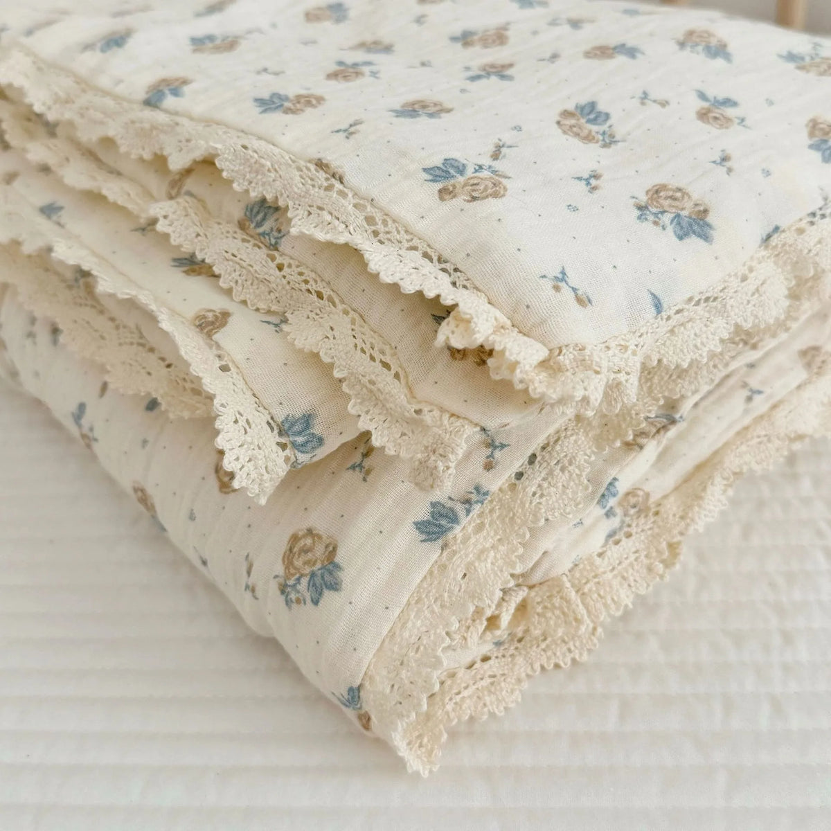 A stack of floral muslin baby blankets in cream and blue floral patterns folded on a white surface.