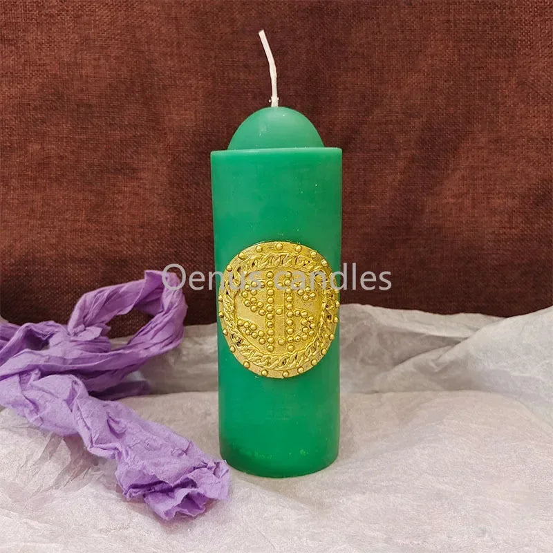 Une grande bougie cylindrique verte avec un médaillon doré, exposée sur un tissu blanc.