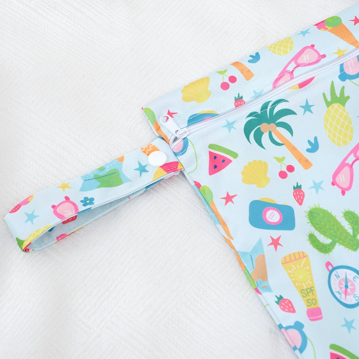 A light blue fabric bag with a colorful tropical fruit pattern and a zipper is shown against a white background.