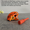 An orange handcrafted wooden frog percussion instrument with a stick, displayed on a gray surface.