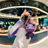 A hand holds a purple plush toy keychain attached to a leather key case in a modern setting.