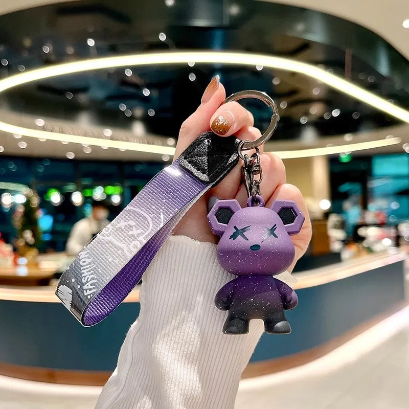 A hand holds a purple plush toy keychain attached to a leather key case in a modern setting.