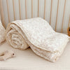 A rolled floral muslin baby blanket in cream and beige tones resting on a light surface.