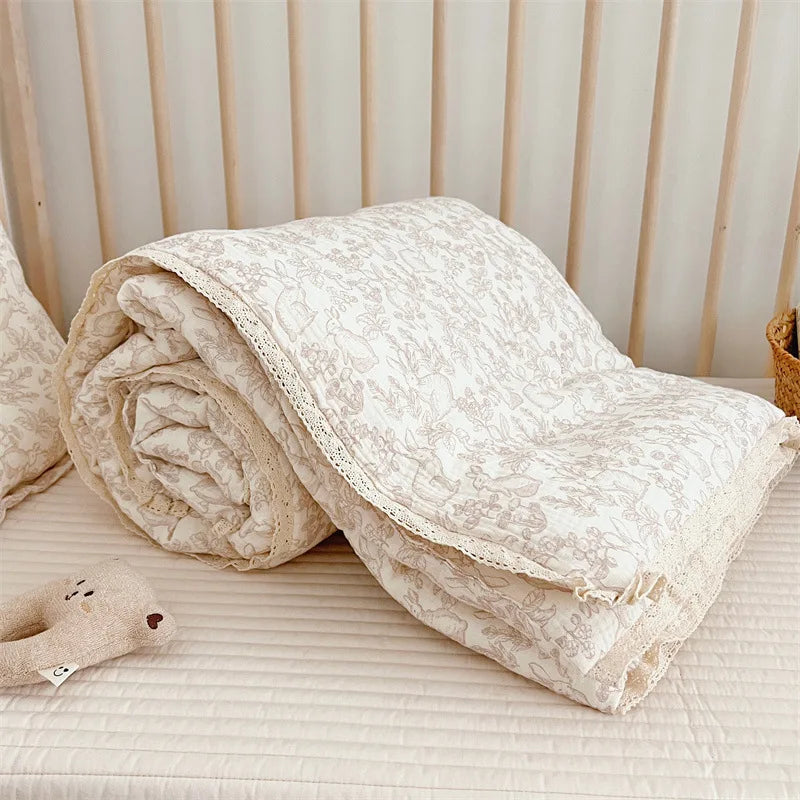 A rolled floral muslin baby blanket in cream and beige tones resting on a light surface.