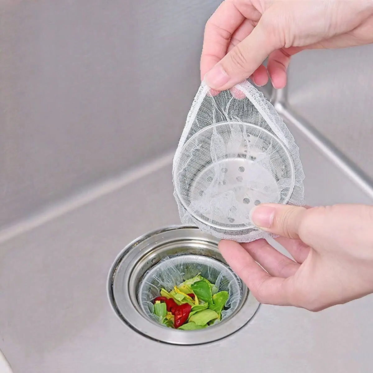 A hand is placing a disposable mesh sink strainer bag filled with vegetables into a metal colander.