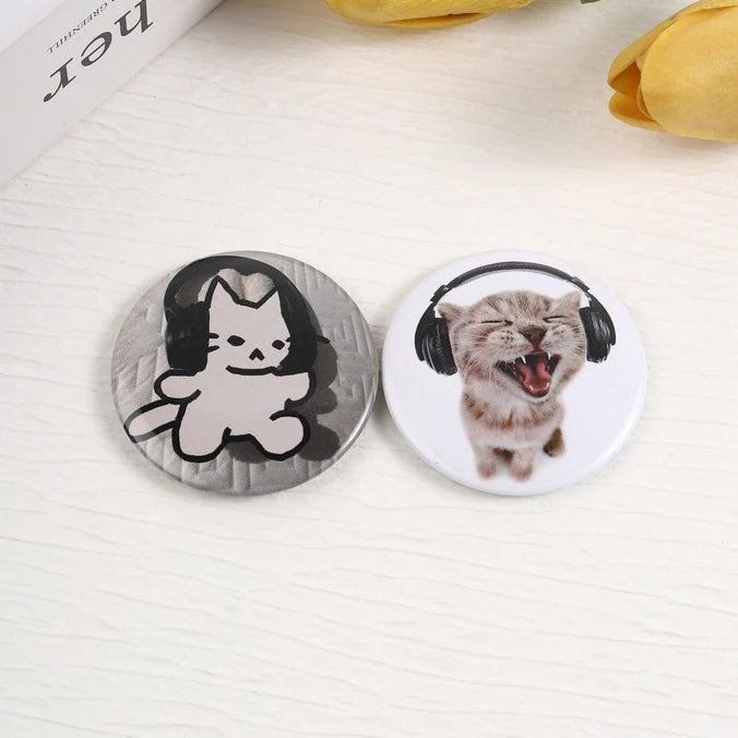 A set of two tinplate pins featuring a black cat and a tabby cat with headphones.