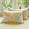 A set of light yellow, white, and sage green cotton pillow shams displayed in front of a window with greenery.