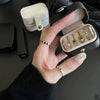 A hand holds an open black leather jewelry travel case displaying various silver and gold rings and earrings.
