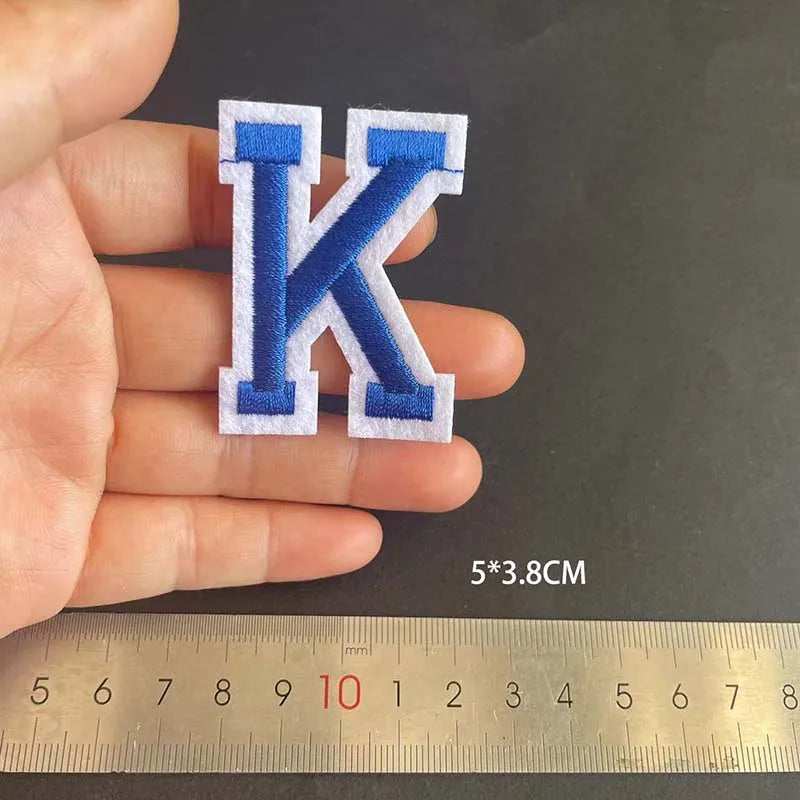 A hand holds a blue and white embroidered letter K patch, measuring 5 by 3.8 centimeters.