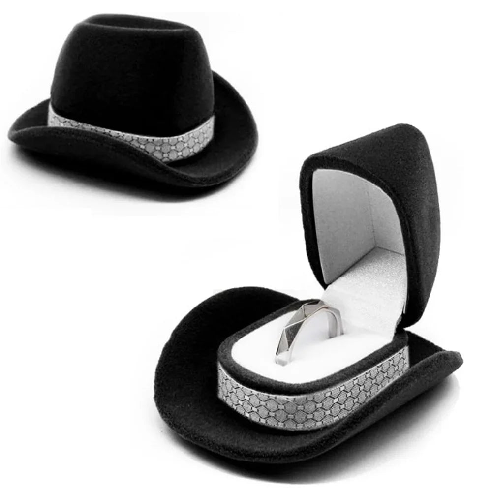 Black felt cowboy hat with silver trim and an open velvet jewelry storage box displaying a ring.