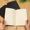 A blank A6 Kraft paper notebook open to show the interior pages on a wooden surface.
