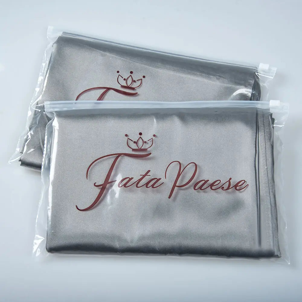 A set of two silky satin pillowcases in gray with a crown design on the fabric.