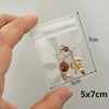 A hand holds a clear plastic jewelry pouch containing gold-toned leaf and bead earrings.
