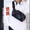 A person wearing a white sweatshirt holds a dark blue tactical chest bag with an orange strap and silver chain.