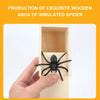 A hand is holding a black spider toy inside a wooden box designed to simulate a spider.
