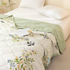 A quilted white and green summer quilt featuring a panda pattern and floral embroidery on a bed.