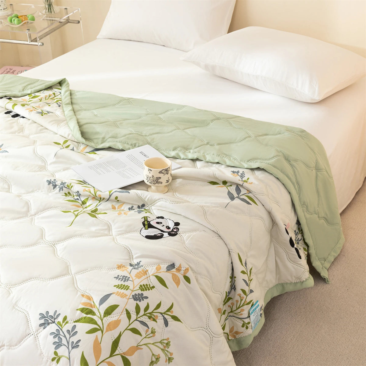 A quilted white and green summer quilt featuring a panda pattern and floral embroidery on a bed.