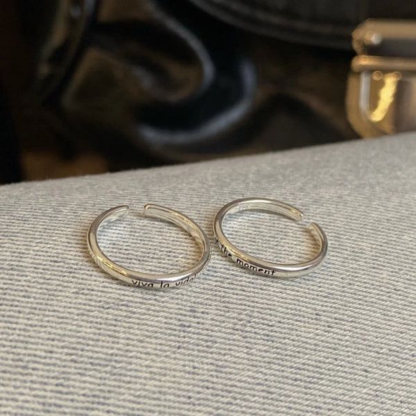 Zwei silberne Ringe mit der Gravur „viva la vida“, ruhend auf einer hellgrauen Oberfläche.