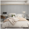 A bedroom featuring a bed with beige linens against a wall covered in vertical light gray wood grain wallpaper.