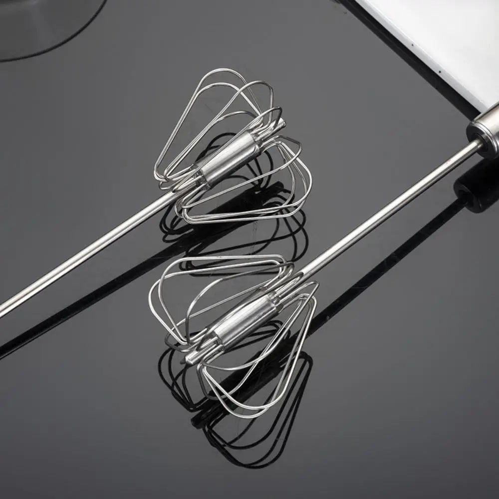 A close-up of three stainless steel manual rotary whisks reflected on a dark surface.
