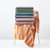 A stack of folded plaid cotton bath towels in various muted colors, with one towel draped over a white hanger.