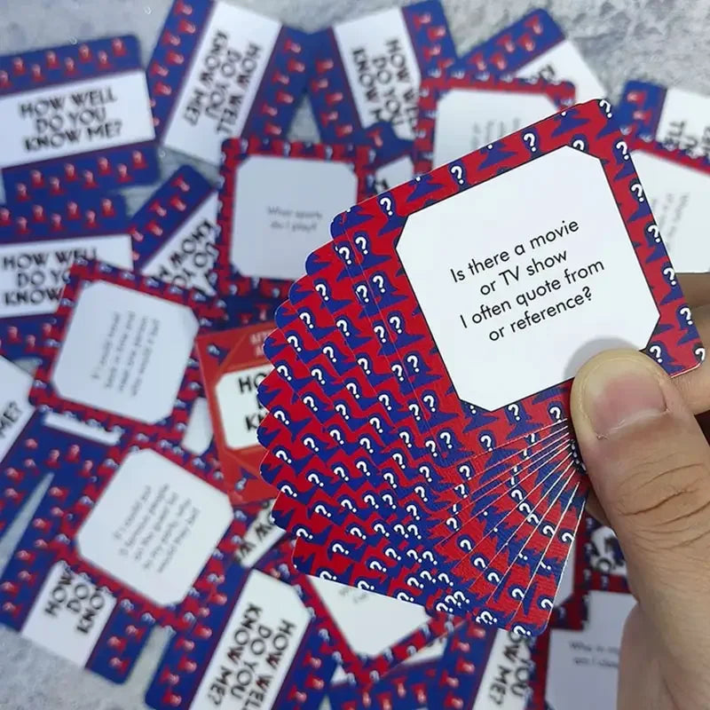 A hand holds a stack of red and blue cards from the How Well Do You Know Me party game.