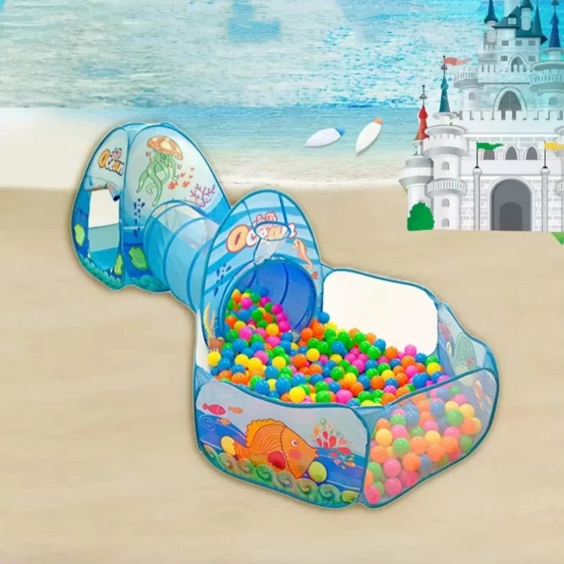 A blue foldable kids play tent featuring a tunnel and ball pit set on a sandy beach background.