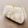 A cream-colored clutch bag featuring delicate pearl embroidery and gold hardware, shown in a profile view.