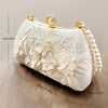 A white clutch bag featuring delicate pearl embroidery and gold hardware, shown in a profile view.