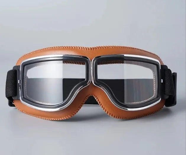 A pair of retro foldable motorcycle goggles in brown leather with silver frames and black lenses.