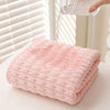 A pink coral velvet bath towel is being filled with water from a clear glass pitcher.