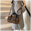 A woman holds a brown leather retro leopard print hobo satchel bag against a light-colored coat.