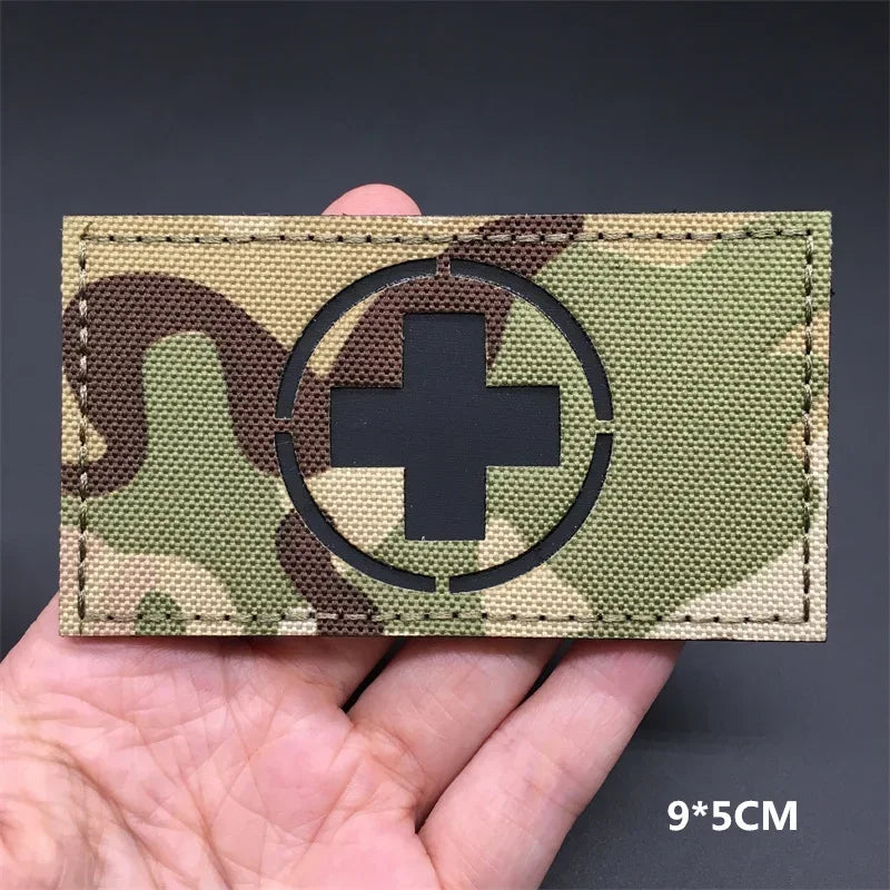 A tactical patch featuring a white cross inside a black circle on a camouflage fabric with hook-and-loop backing.