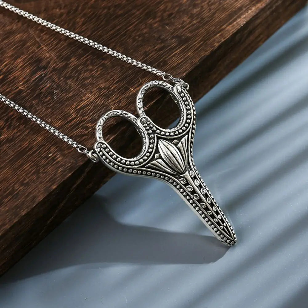 Vintage stainless steel sewing scissors with a chain resting on a dark wooden surface.