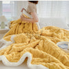 A fluffy yellow fleece throw blanket draped over a bed, showing its thick texture and white trim.