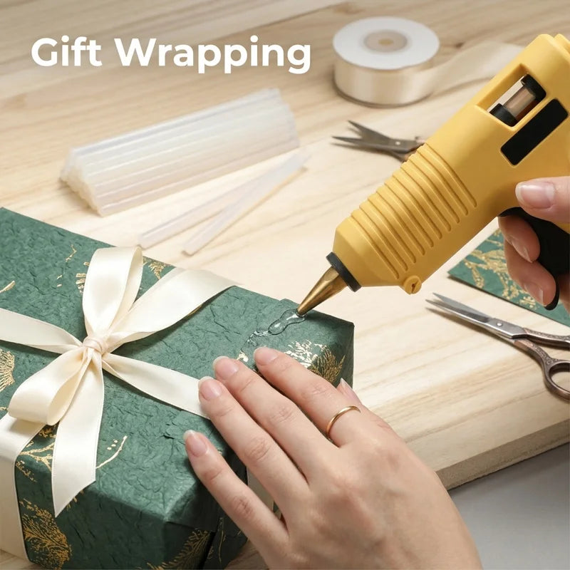 A hand uses a yellow hot glue gun to apply clear glue to a gift box for wrapping.