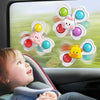 A baby is looking at a window showing colorful spinning bath toys with flower shapes and animals.