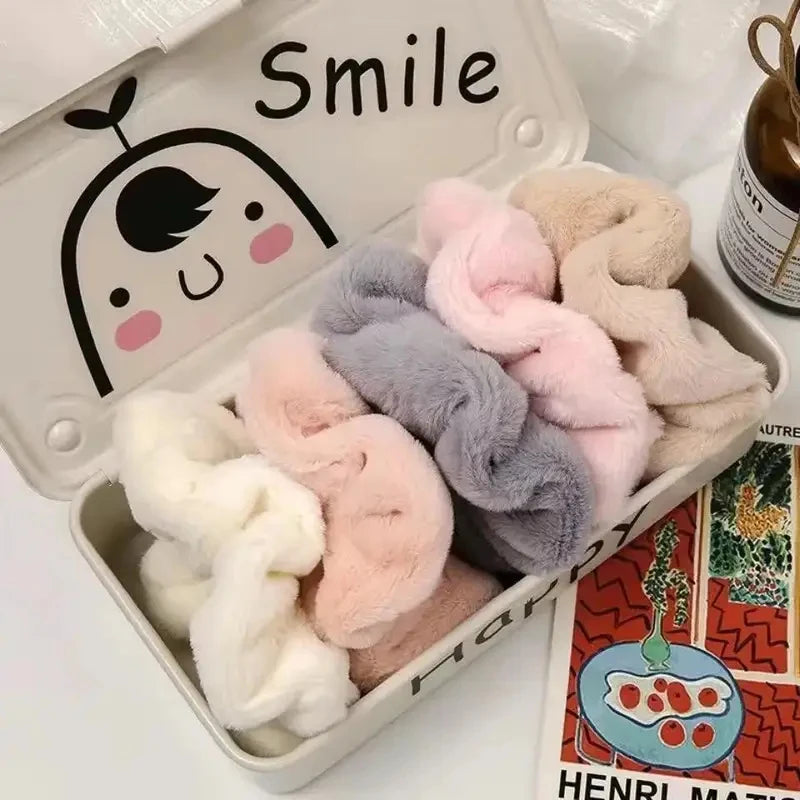 A collection of soft, fluffy coil hair ties in pastel shades including pink, lavender, and beige, displayed in a white box.