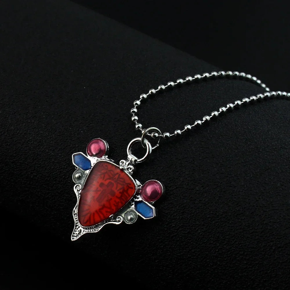 A silver pendant necklace featuring a red stone and small blue and pink beads.