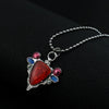A silver pendant necklace featuring a red stone and small blue and pink beads.