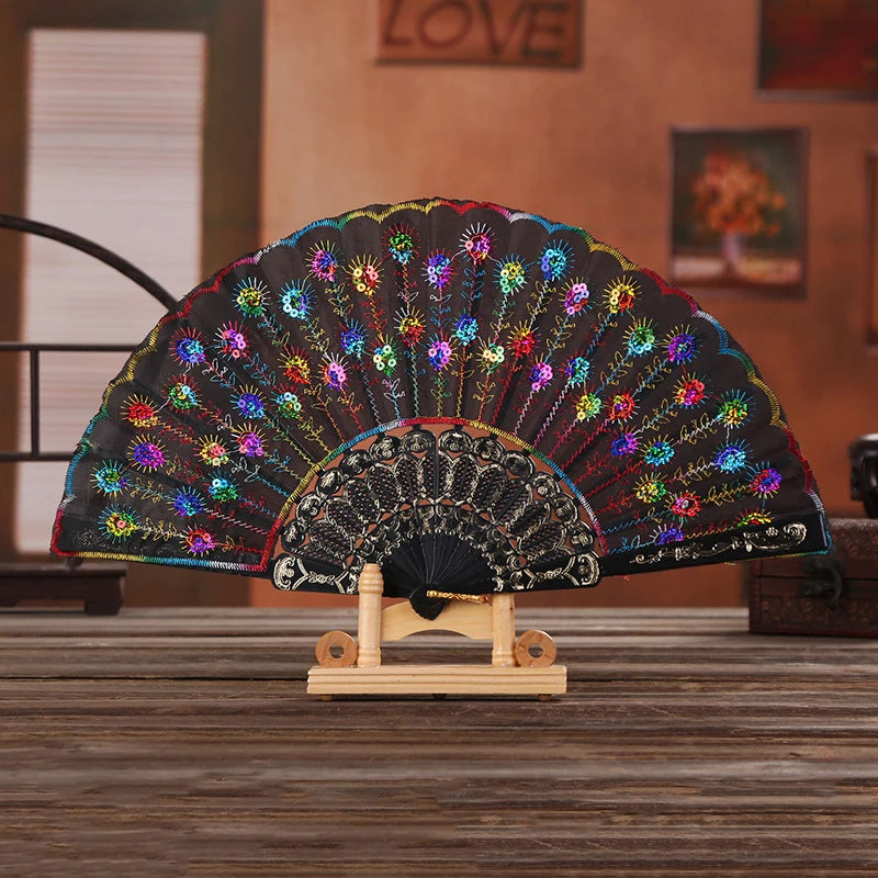 A black and multicolored bamboo and silk folding fan with a floral design displayed on a wooden stand.