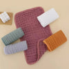 A stack of five colored muslin baby burp cloths including white, green, purple, and orange shades.